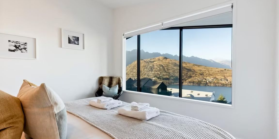 Bedroom with layered pillows, looking out to a lake and snow-capped mountains