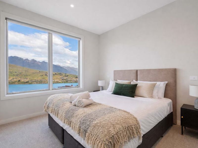 Bedroom with a bay window overlooking the lake and mountains, styled with a knit throw and folded towels