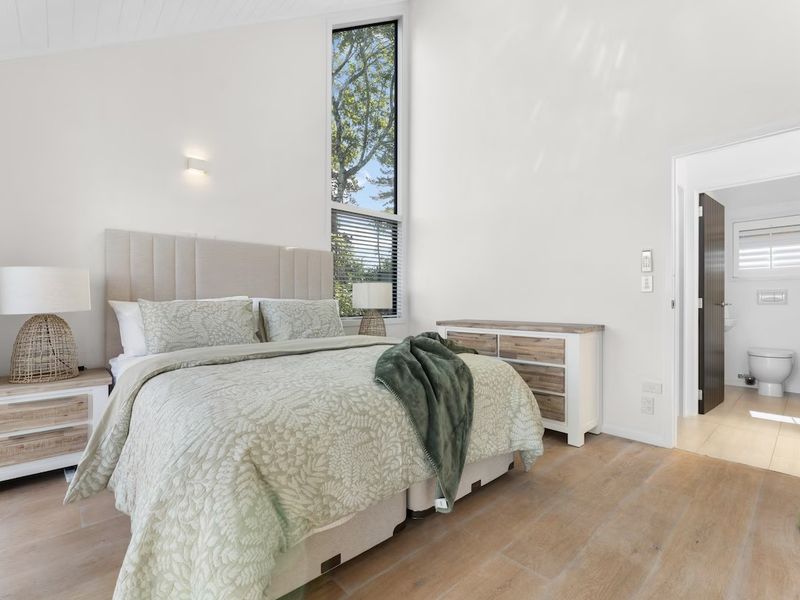 Bedroom with sage green bedding, tall windows and an ensuite bathroom
