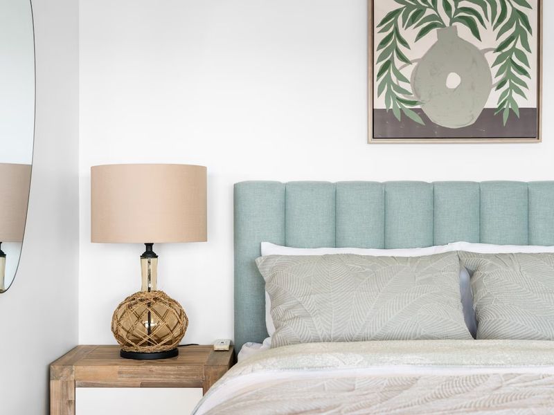 Headboard detail with a botanical print and woven bedside lamp