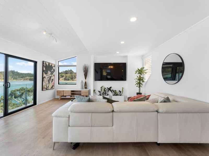 Open-plan living room with floor-to-ceiling glass doors framing the sea and native bush