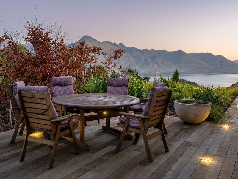 Outdoor dining setting on a deck overlooking mountains and a lake at sunset